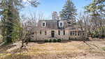 A beige two-story house with dormer windows and a steep roof sits among leafless trees on a patchy, brown lawn under a blue sky at 602 Williamsboro Street in Oxford.