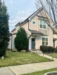 A two-story beige house with white trim, large windows, and a small covered entryway at 107 York Drive in Oxford, surrounded by shrubs, trees, and a neatly maintained lawn along a concrete sidewalk.