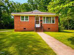 A small, single-story brick house at 209 Lee Street, Oxford, features a grassy lawn, concrete walkway and steps to the front door. Large windows flank the entrance; trees and greenery surround the home on a bright, sunny day.