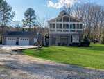 Modern two-story house at 301 Pebble Hill Lane in Henderson with large upper-floor windows, an attached three-car garage, outdoor patio with pergola, and a well-maintained lawn surrounded by trees on a sunny day.