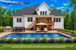 A modern two-story white house at 190 Whistlers Cove, Louisburg, features a large deck overlooking a rectangular swimming pool and patio area. Outdoor furniture and a grill sit near the pool, with trees, blue sky, and green lawn completing the scene.
