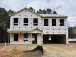 A two-story house under construction at 20 Buckthorn Drive, Youngsville, is covered in white building wrap with exposed window openings and an unfinished roof. The dirt lot features a visible double garage, front porch, and trees in the background.