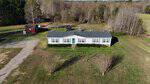 Aerial view of a single-story light gray house with dark roof at 455 Swansons Road, Louisburg. Surrounded by grass and trees, it features a backyard shed, trampoline, and a dirt driveway leading to the home.