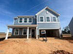A newly constructed two-story blue house with white trim and a covered front porch sits at 13 Lotus Bend Way, Youngsville, on a dirt lot awaiting landscaping. A construction sign stands in front of the garage.