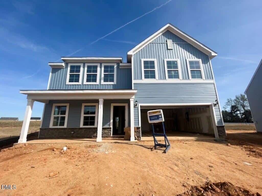 A newly constructed two-story blue house with white trim and a covered front porch sits at 13 Lotus Bend Way, Youngsville, on a dirt lot awaiting landscaping. A construction sign stands in front of the garage.