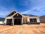 A newly constructed single-story house at 145 Sugarmaple Way in Youngsville with white siding, dark gables, and stone accents, featuring an attached garage and a front porch, set on a dirt lot under a blue sky.