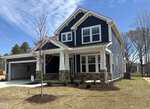 A modern two-story house with blue siding, white trim, a covered porch, and an attached garage at 215 Sugar Pine Drive in Franklinton. The front yard features young trees, shrubs, fresh landscaping, and a clear blue sky overhead.