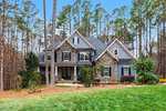 Charming two-story house at 3587 Garner Terrace Way, Wake Forest, with stone and blue siding, gabled roof, and multiple windows, nestled among tall pine trees and landscaped lawn with shrubs and mulch under a clear blue sky.