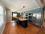 Modern kitchen at 204 Winston Street, Franklinton, featuring blue cabinets, stainless steel appliances, a dark-based center island with granite countertop, pendant lights, hardwood floors, and large windows for abundant natural light.