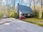 A cozy two-story house at 201 Hillandale Drive, Oxford, features a steep green roof, white siding, and a brick chimney, surrounded by trees and shrubs with a detached garage along a quiet paved road.