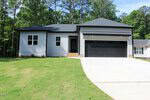 A modern single-story house at 116 Mohave Drive, Louisburg, featuring light gray siding, black trim, a dark roof, double garage doors, a sloped driveway, freshly planted lawn, and trees in the background.