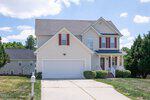 A two-story suburban house at 1976 Sadler Avenue in Creedmoor features cream-colored siding, red shutters, a front porch, and a double garage. A white mailbox sits by the driveway, with trimmed bushes lining the yard on a sunny day.