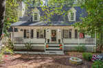 A white house at 170 Misty Way in Franklinton features a front porch, black shutters, and dormer windows, decorated with autumn wreaths and pumpkins. An American flag hangs by the steps, and a fire pit sits in the yard surrounded by trees.
