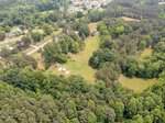 Aerial view of a green, tree-filled landscape in Franklinton with open grassy areas, scattered houses, and roads winding through a suburban neighborhood. Dense forest surrounds the central clearing near 695 W Green Street.