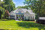 Located at 25 Winchester Court in Youngsville, this beige two-story suburban house features black shutters and a red front door, surrounded by a lush lawn, mature trees, and landscaped beds along a curved walkway.