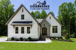 A white modern farmhouse with a gable roof, black trim, and front porch sits on a green lawn in Louisburg at 295 Whistlers Cove. Trees frame the background, with the "Colebrooke Custom Homes" logo displayed above the house.