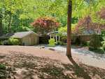 A single-story house at 206 Beechwood Trail in Henderson features a two-car garage, surrounded by lush green trees and shrubs, with sunlight filtering through the leaves onto the driveway and front yard.