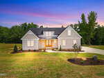 Modern farmhouse-style home at 25 Serenity Woods Trail in Franklinton, featuring white board and batten siding, black roof, large windows, and a front porch set against a vibrant sunset sky with trees and landscaped yard.