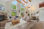 A spacious living and dining area at 110 Mohican Drive in Louisburg features vaulted ceilings, exposed wooden beams, large windows, a fireplace, beige sofas, armchairs, a wooden coffee table, dining set, and mounted deer heads on the walls.