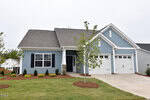 Charming single-story house at 68 Moon Flower Walk, Youngsville, with blue siding, white trim, black shutters, and a dark gray roof. Features two white garage doors, a cozy front porch, and young trees in the landscaped yard.