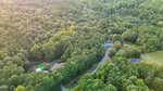 Aerial view of houses in Louisburg, surrounded by dense, green forest, with a winding road and two round pools in backyards near 87 Beaver Court, taken on a sunny day.