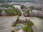Aerial view of a house on Lot 6 W River Road in Franklinton, surrounded by wintery fields and leafless trees, with a dirt path leading into dense forest and scattered debris near the property.