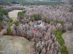 Aerial view of Lot 7 W River Road, Franklinton: a small pond encircled by dense, leafless trees and patches of green pines. Open grassy fields border the woods, with a forest stretching into the distance.