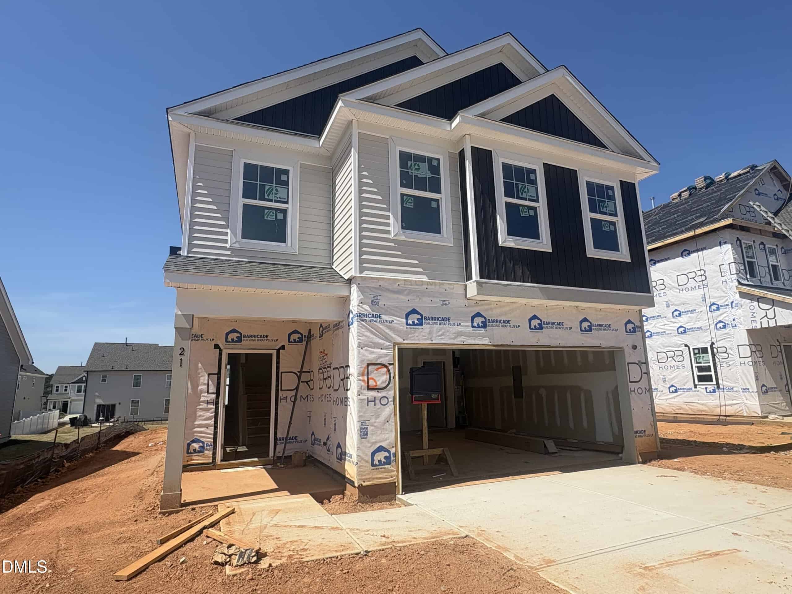 A newly constructed two-story house at 21 Gerrard Street in Franklinton features white and dark gray siding, an unfinished driveway, exposed garage interiors, and construction materials scattered on bare red soil. Other houses are visible nearby.