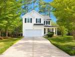 A two-story white house with black shutters and a double garage sits at the end of a wide driveway on 1991 Ferbow Street in Creedmoor, surrounded by green grass, trees, and a clear blue sky.
