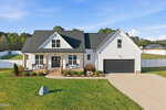 A modern white house with black roof and garage at 150 Eagle Chase Drive, Youngsville, featuring a front porch with chairs, neatly landscaped yard, large driveway, and set against green grass, trees, and a blue sky.