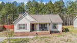 A single-story house at 204 Orkney Road in Stem features beige siding, a brick foundation, and a covered front porch with chairs, set against tall pine trees and a partially fenced yard.