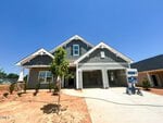 A newly constructed gray house with white trim at 76 Moon Flower Walk, Youngsville, features a covered front porch, double garage, fresh landscaping, and a small tree planted near the driveway under a clear blue sky.