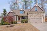 A two-story suburban house at 201 Petal Grove Court, Youngsville, features a mix of stone and siding exterior, peaked roofs, a front porch, and an attached two-car garage. Brown summer grass and landscaped bushes complete the inviting front yard.