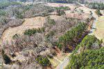 Aerial view of a rural landscape near 3018 NC 56 in Creedmoor, with a winding road, dense green trees, open fields, and a few scattered buildings among the trees. Forested areas and farmland stretch into the distance.