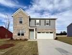Two-story suburban house at 212 Blue Sky Lane, Louisburg with brick and gray siding exterior, light blue front door, double garage, and large driveway. The yard features fresh landscaping and a small tree beneath a blue sky with clouds.