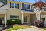 A beige two-story townhouse with white trim at 1429 Montonia Street, Wake Forest, features a covered entryway, green shrubs, a small tree, and a concrete pathway leading to the front door on a sunny day.