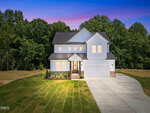 A two-story modern house with white siding at 75 Basil Court, Franklinton, features a front porch and double garage, set on a large, neatly manicured lawn with a wooded area in the background at sunset.