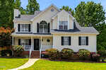 Charming two-story suburban house at 2634 Bowden Drive, Creedmoor, with white siding, black shutters, and a brick foundation. Enjoy the front porch with white railings and a landscaped yard surrounded by tall green trees.