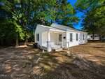 Charming small white single-story house at 846 State Street in Henderson, featuring a covered front porch, shaded by trees with a dirt yard. Steps lead up to the quiet residence, perfect for enjoying sunny outdoor surroundings.