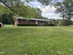 A single-story brick house at 4509 Cannady Mill Road in Oxford sits on a large, grassy yard with trees in the background and partly cloudy sky overhead. Shrubs line the front of the house, and a small porch is visible at the entrance.