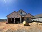 A house under construction at 85 Moon Flower Walk, Youngsville, with exposed framing and house wrap. The garage sits on the left, piles of lumber in front, and bare dirt surrounds the site under a clear blue sky.