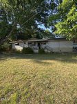A single-story, light-colored house at 105 Layton Street in Franklinton features a covered front porch behind a patchy lawn, shaded by large trees on a sunny day. Bushes line the porch, with shadows falling across the yard.