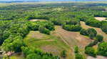 Aerial view of a rural Creedmoor landscape with rolling green hills, dense forested areas, open grassy fields, and scattered patches of trees near 0 Pope Road under a hazy sky.