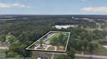 Aerial view of a rectangular property at 3845 Raleigh Road in Henderson, outlined in white, featuring several buildings, trees, and open land, surrounded by roads, houses, and forested areas under a partly cloudy sky.