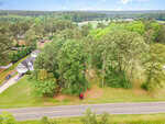 Aerial view of a wooded lot with tall trees next to a paved road at 63 Mount Olivet Church Road, Franklinton. A red car is parked under the trees, and a white house with a driveway is visible to the left, with more trees and a park-like area in the background.