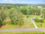 Aerial view of 71 Mount Olivet Church Road in Franklinton, featuring a rural road with a driveway leading to a house nestled among trees, open grassy areas, and a wooded forest under a partly cloudy sky.