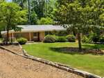One-story brick house with large windows at 291 Williamsboro Street, Oxford. Surrounded by trees and shrubs, the yard features a green lawn, mulch, and a stone-lined path. Bright, sunny day with a wooded area in the background.