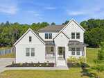 A modern two-story white house at 230 Scotland Drive, Youngsville, with a covered front porch, manicured landscaping, and a green lawn, set against a backdrop of trees and blue sky.