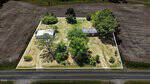 Aerial view of 42 Collie Road, Castalia: a fenced rectangular property with two small buildings, several trees, and grassy patches, surrounded by plowed farmland and bordered by a paved road in the foreground.