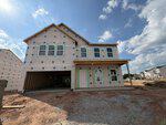 A two-story house under construction at 49 Plantation Drive, Youngsville, with unfinished exterior walls, exposed framing, and a covered garage. Bare soil and gravel surround the site, with other homes visible under a partly cloudy sky.